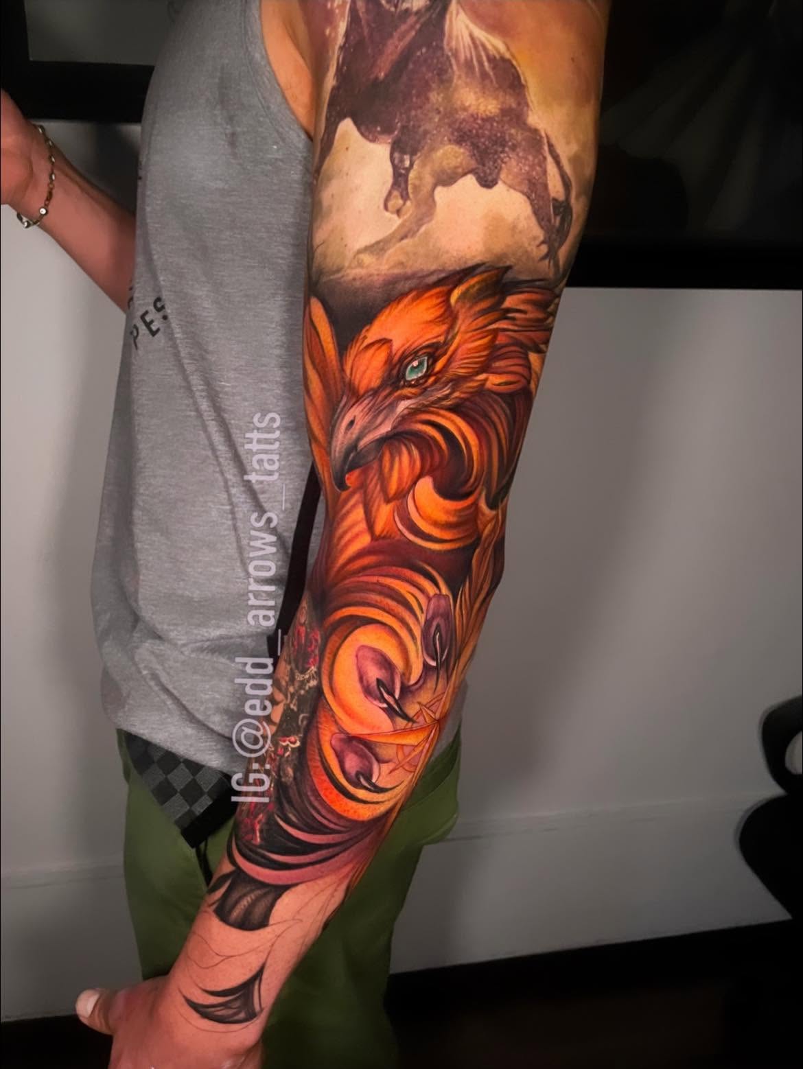 Full-sleeve tattoo of a phoenix with a teal eye, orange and gold feathers sweeping down the arm
