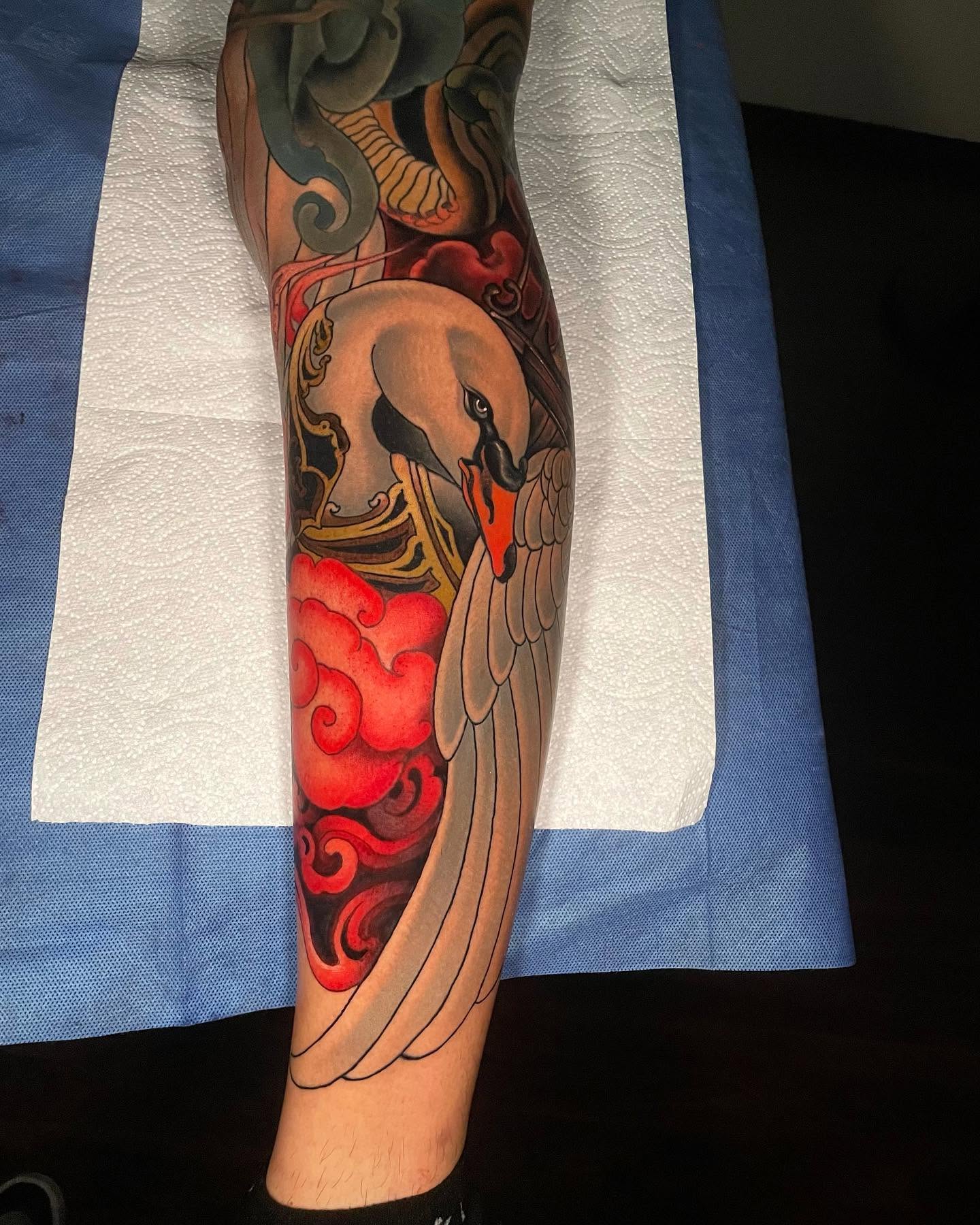 Lower-leg tattoo of a swan with folded wings over bright red clouds, neo-traditional color