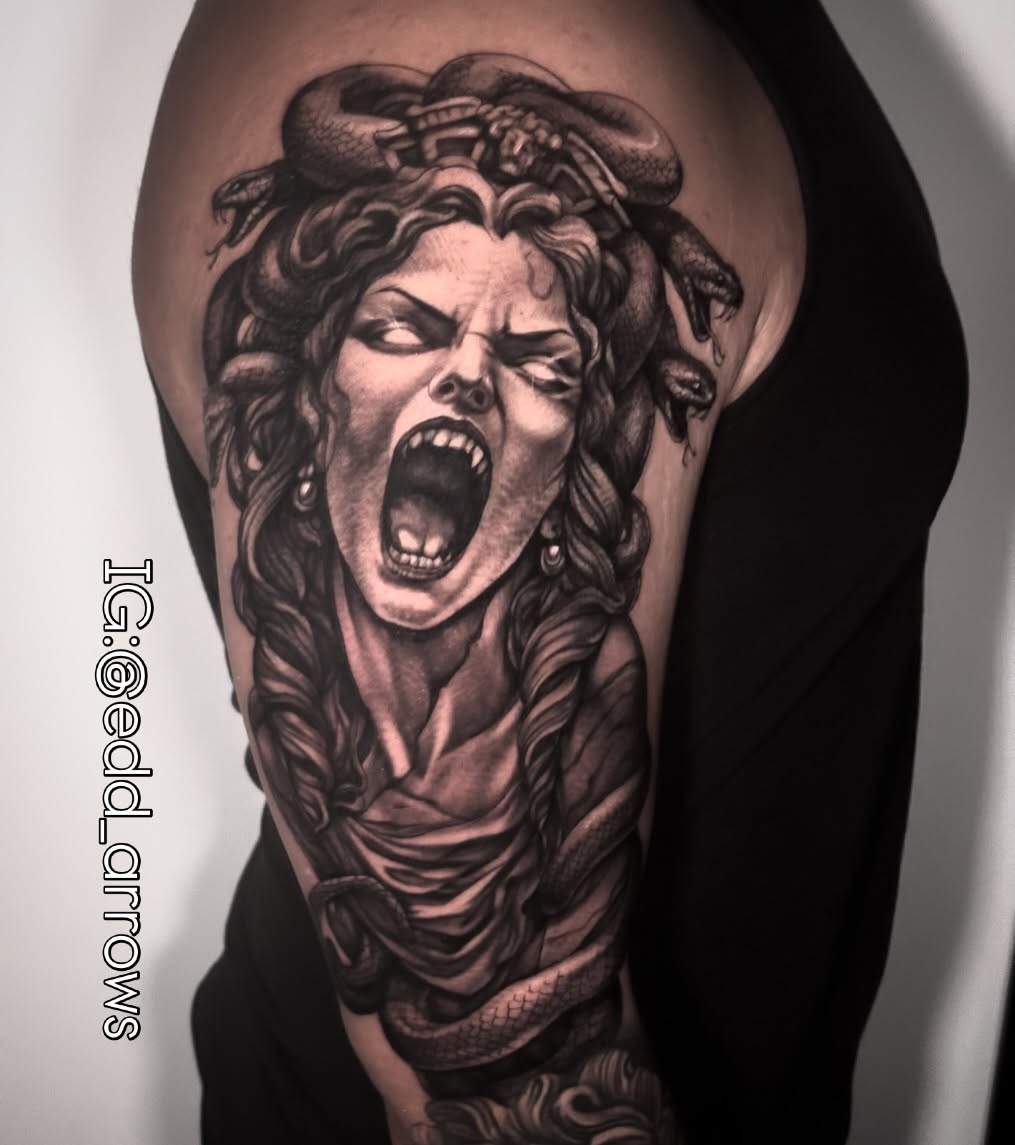 Black and grey upper-arm tattoo of Medusa screaming, snakes coiling through her hair